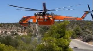 Firefighting helicopter scooping water from an ASKOMET tank to extinguish the fire in Koropi, Attica.